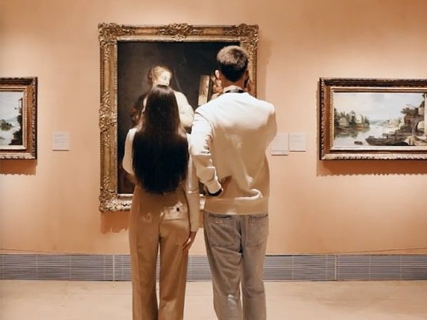 Una chica y un chico de espaldas observando un cuadro mientras escuchan la audioguía