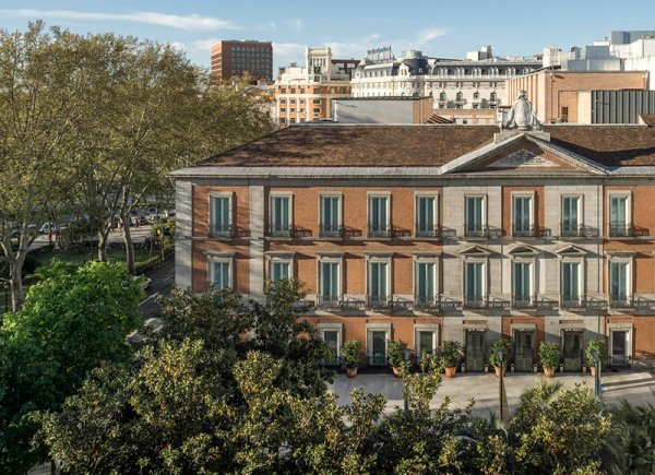Fachada del Museo Nacional Thyssen-Bornemisza entre árboles, con edificios de Madrid al fondo